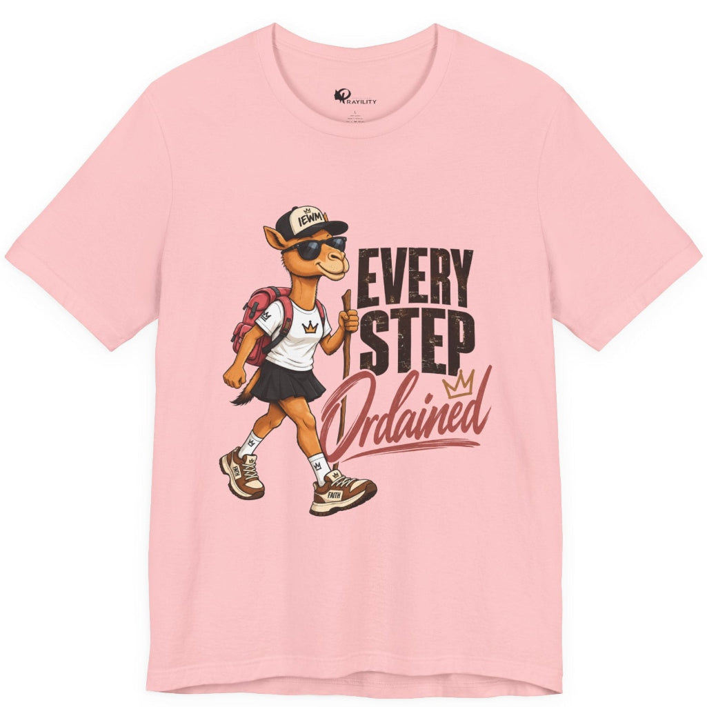 A light pink short-sleeve crewneck T-shirt featuring a graphic print of a walking camel mascot wearing sunglasses and a cap next to the text 'EVERY STEP Ordained'.