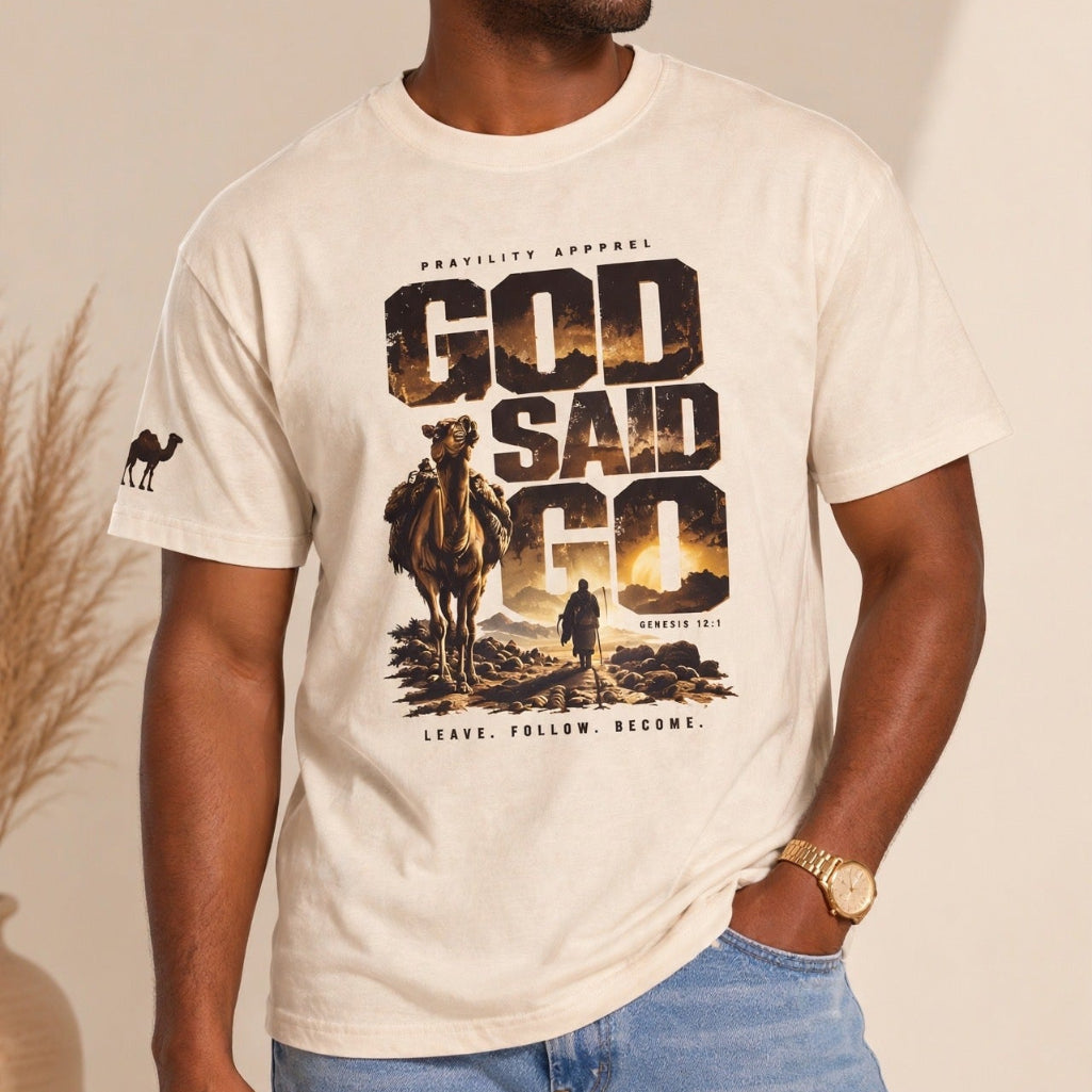 A man wearing a cream-colored graphic t-shirt with a camel and 'GOD SAID GO' print, paired with light blue jeans, standing against a warm beige background.