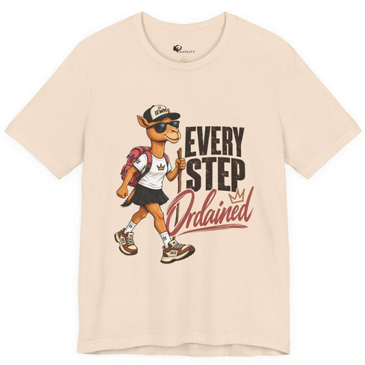 A light beige crewneck t-shirt featuring a graphic print of a walking camel mascot wearing sunglasses and a cap next to the text 'EVERY STEP Ordained'.