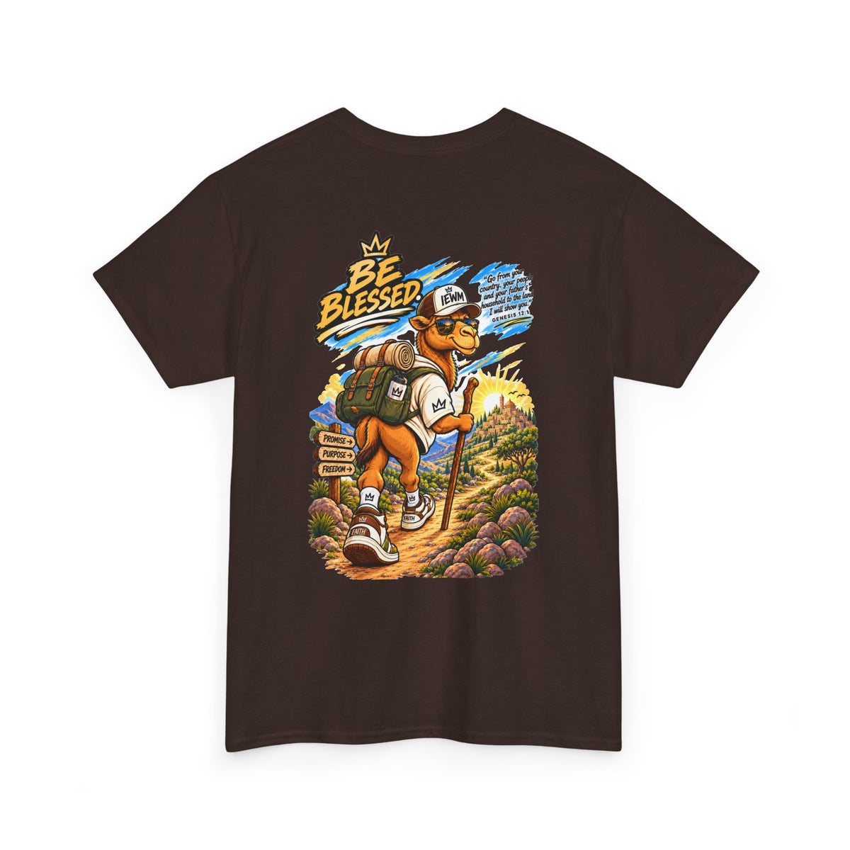 A dark brown short-sleeve t-shirt with a colorful graphic print on the front. The graphic features a cartoon hiking camel wearing a 'IEWM' hat and backpack, set against a scenic mountain background with text that reads 'BE BLESSED'.